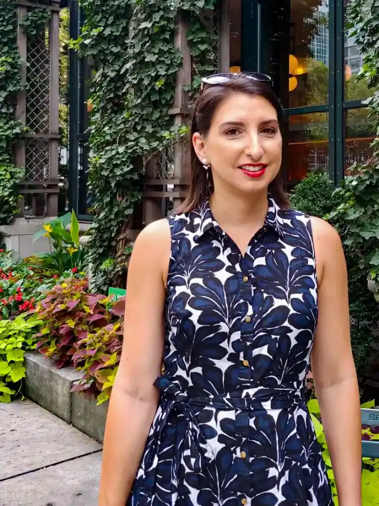 Elegant woman in a navy and white floral sleeveless dress standing outdoors amidst vibrant garden greenery, ideal for keto lifestyle, health-conscious living, and fashion inspiration.