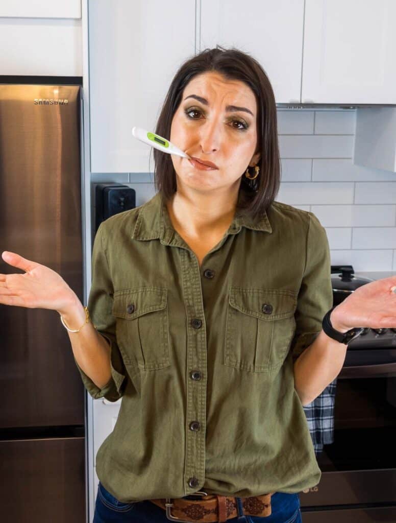 Frustrated woman with a thermometer in her mouth, neglecting her health, in a modern kitchen setting.