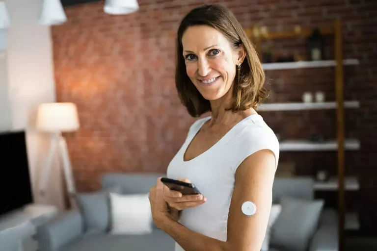 Woman over 40 wearing a continuous ketone monitor on her arm while using a smartphone at home